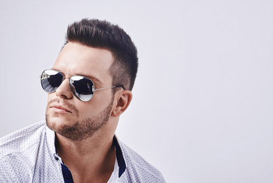 Closeup Portrait Of A Casual Young Man With Sunglasses Looking At The Camera. On Gray Background