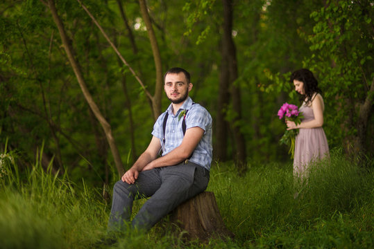 Man sits on the stump and woman stands far away back of him