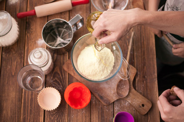 Mother and daughter hands  preparing the dough on the table. Ingredients and devices for cup-cake on a wooden background. House pastries. Food concept. Flour, eggs, butter, mix for pastries. Top view