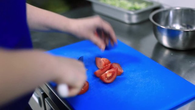 Chef cuts the tomato in the kitchen of the restaurant