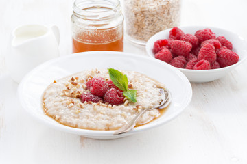 plate of oatmeal with fresh raspberries and honey on white table
