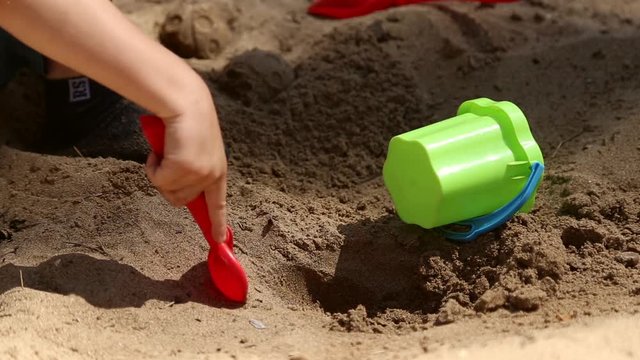 A boy plays in the sandbox with shovel and pail and shapes for sand