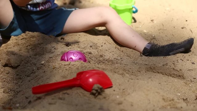 A boy plays in the sandbox with shovel and pail and shapes for sand