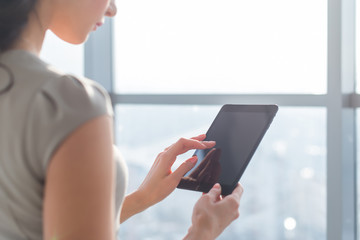 Side view photo of young female teleworker using tablet, searching and browsing information via wi-fi connection application in office or at home.