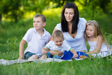 Happy mother, two sons and daughter dressed in white shirts are sitting on the grass in the park