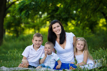 Happy mother, two sons and daughter dressed in white shirts are sitting on the grass in the park