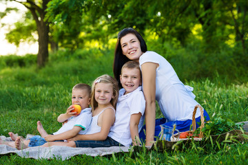 Fototapeta premium Happy mother, two sons and daughter dressed in white shirts are sitting on the grass in the park