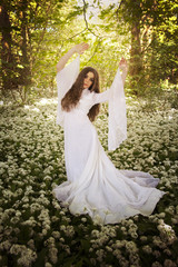 Beautiful woman in long white dress standing in a forest on a car