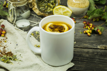 Cup of tea on wooden background with lemon and herbs