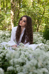 Fototapeta na wymiar Beautiful woman wearing a long white dress sitting in a forest 