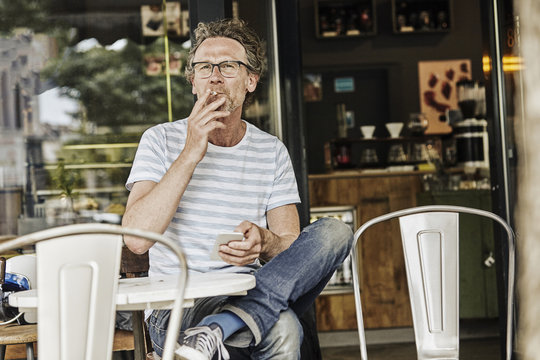 Smoking man sitting in front of a coffee shop