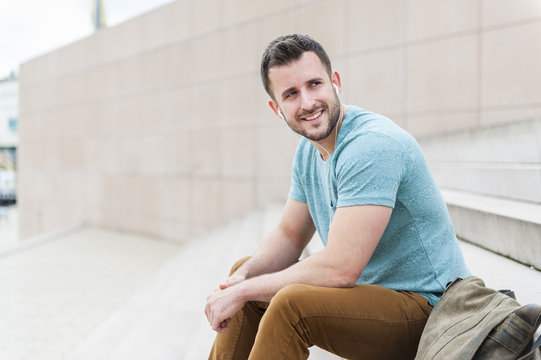 Smiling young man outdoors sitting on stairs listening to music