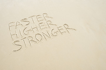 Motivational Faster Higher Stronger message handwritten in smooth sand