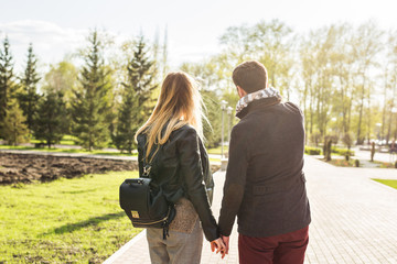 love, relationship, family and people concept - young couple holding hands in autumn park from back