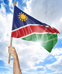 Person's hand holding the Namibian national flag and waving it in the sky, 3D rendering