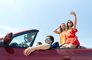 friends driving in cabriolet car and taking selfie