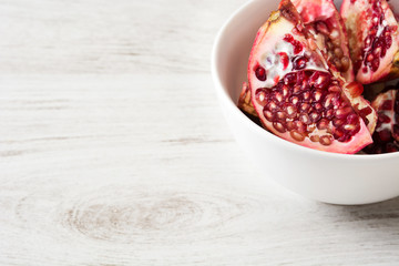 Pomegranate in bowl on white wooden background

