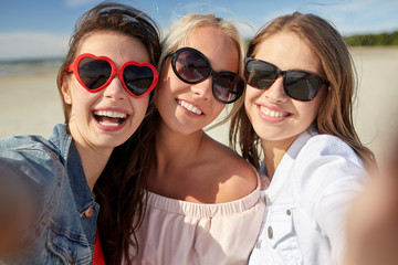 group of smiling women taking selfie on beach