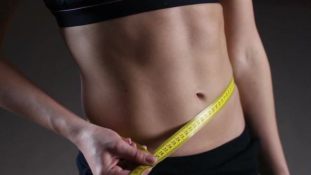 Sportive lady measuring waist after weightloss diet and active training in gym