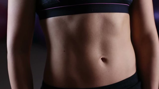 Young woman demonstrating flat tummy muscles, result of active workouts in gym