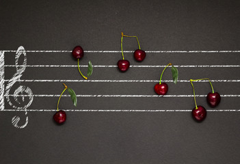Sweet music / Creative concept photo of an illustrated musical staff with cherries as notes on black background.