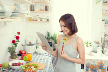 Asian young woman eating healthy food and using a tablet compute