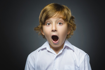 Closeup Portrait of handsome boy with astonished expression while standing against grey background
