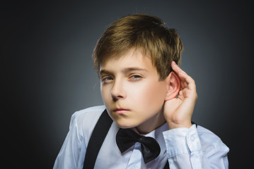 Curious Disappointed boy listens. child hearing something, parents talk, hand to ear gesture isolated grey