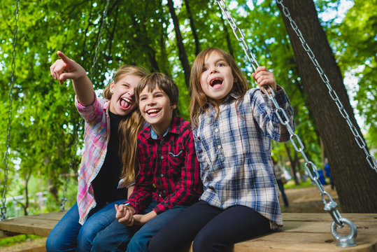 Smiling kids having fun at playground. Children playing outdoors in summer. Teenagers riding on a swing outside