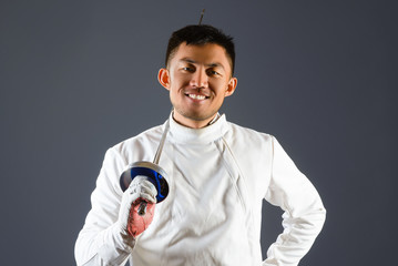Fencing athlete posing with a sword or epee on gray background