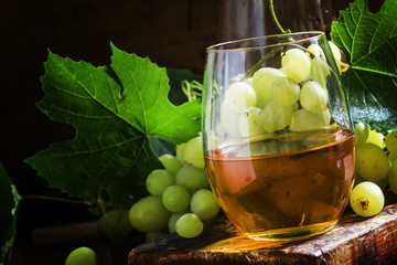 White wine in a glass, green grapes with leaves in a wine cellar