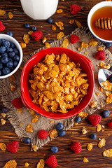 Corn Flakes with berries raspberries, blueberries, glass of milk, and sweet honey.