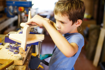 boy making model airplane made of wood. child doing crafts of wood in the workshop