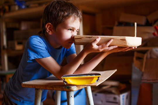 boy builds a toy ship of wood. child in the workshop makes crafts. toy boat of wood