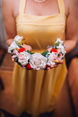 A woman holding a wreath close up hand indoor. Woman in yellow dress. A wreath of white roses closeup. The bride gives white roses