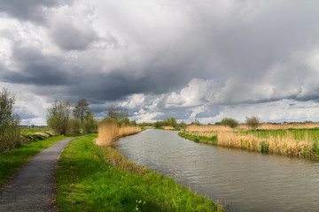 Fototapeta na wymiar Bike path along canal. Beautiful skies on a spring day.