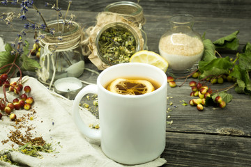 Cup of tea on wooden background with lemon and herbs