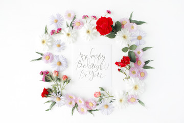 inspirational quote "be happy, be bright, be you" written in calligraphy style on paper with pink, red roses, chamomiles and leaves isolated on white background. Flat lay, top view
