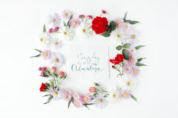 inspirational quote "everyday is a new adventure" written in calligraphy style on paper with pink, red roses, chamomiles and leaves isolated on white background. Flat lay, top view