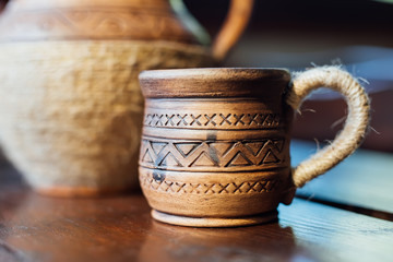 Pitcher and Cup of red clay with Ukrainian ornament on the wooden table