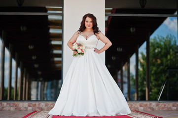 Naklejka premium Big breasts brunette bride with wedding bouquet posed at wedding