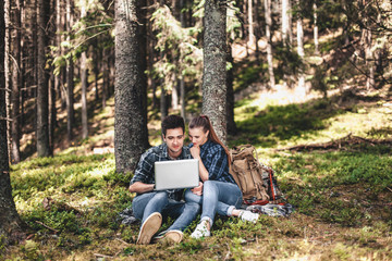 Fototapeta premium A couple of tourists sitting and looking at laptop in the woods. The concept of active rest