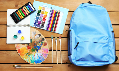 School set with backpack, shoes and supplies on wooden background