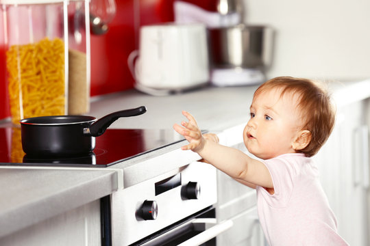 Little child playing with pan and electric stove in the kitchen