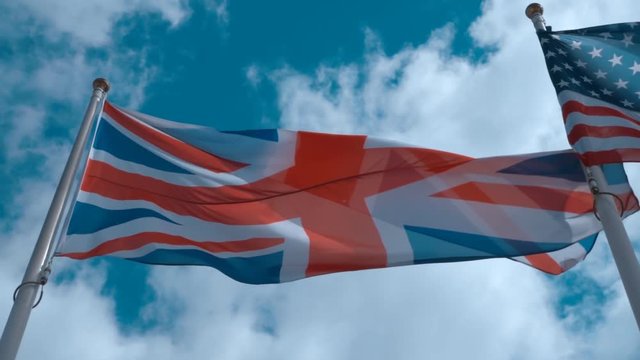 American and English flags on the flagpoles waving in the wind against a blue sky with clouds. Slow motion, high speed camera, 250fps