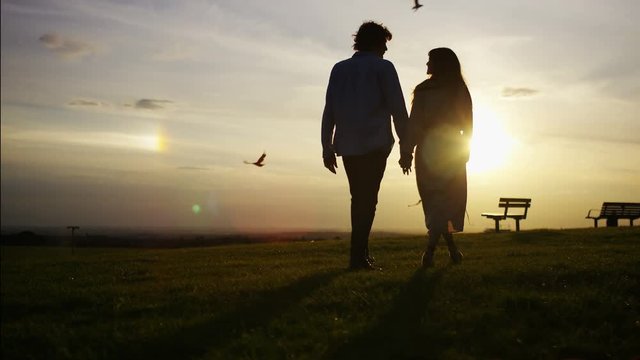 4K Silhouette couple walk towards the sunset holding hands, in slow motion