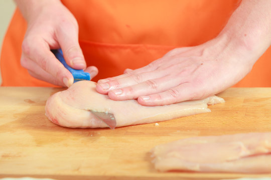 Man cutting raw chicken meat on wooden board