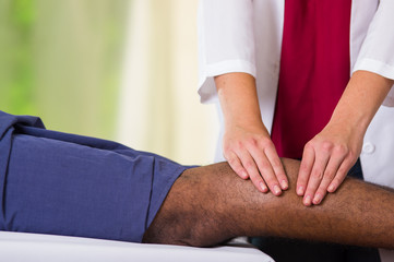 Man getting physical leg treatment from physio therapist, her hands working on his calves applying massage, medical concept