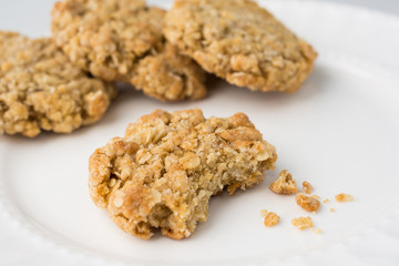 Four oatmeal cookies with bite and crumbs on white plate