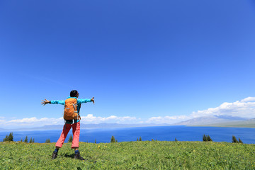 cheering young woman backpacker open arms at mountain peak
